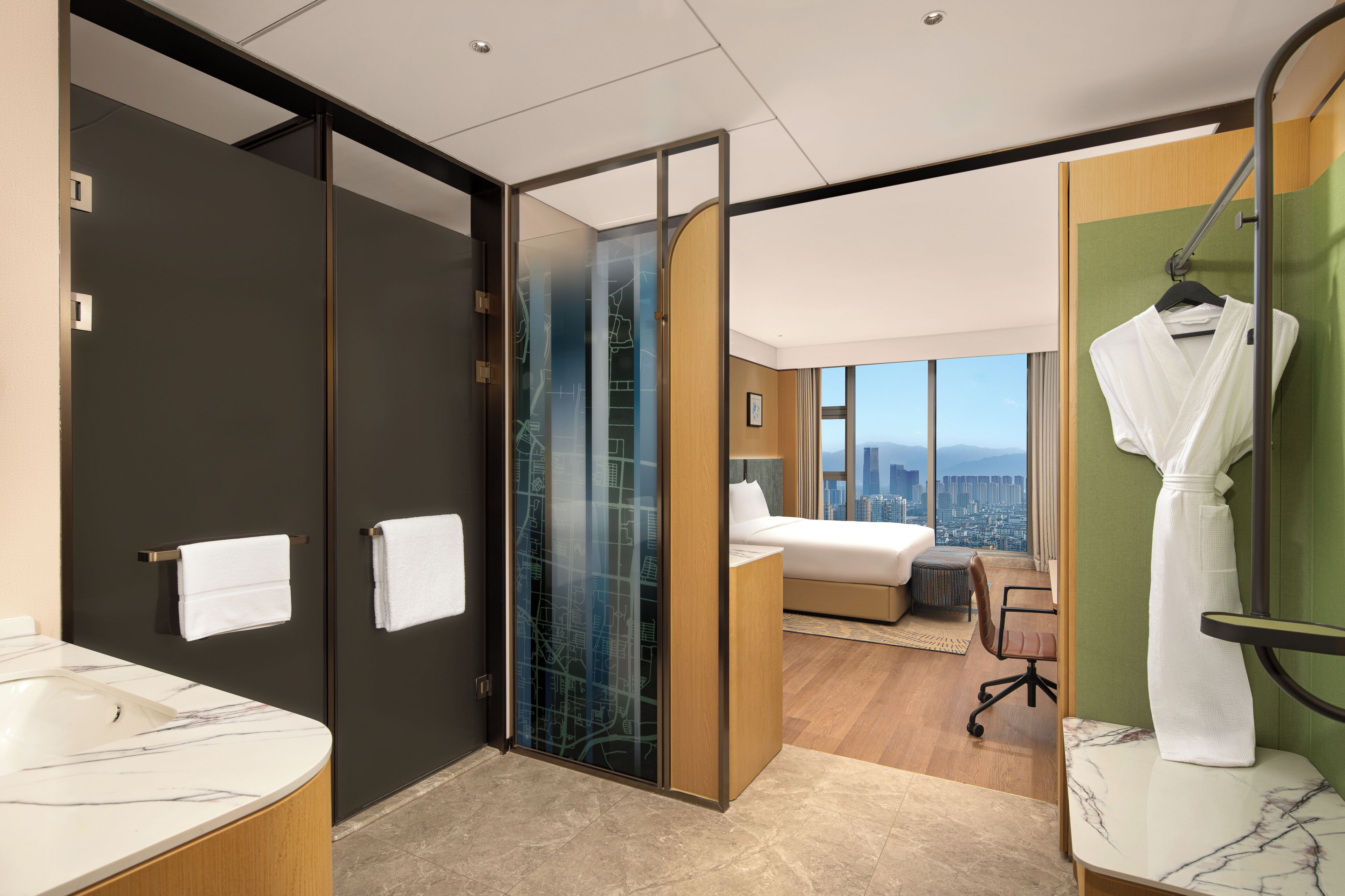 A modern hotel room with a bathroom, a bed, a robe, and a city view.