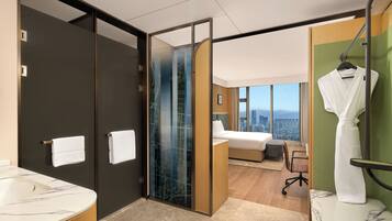 A modern hotel room with a bathroom, a bed, a robe, and a city view.