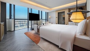Una habitación de hotel moderna con una cama grande, un televisor de pantalla plana, un sofá, un escritorio y vistas a la ciudad.
