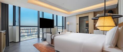 Quarto de hotel moderno com uma cama grande, televisão de tela plana, sofá, escrivaninha e vista para a cidade.