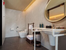 Un baño moderno con inodoro, bidé y lavamanos, equipado con un pasamanos y un perchero para toallas.