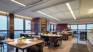 Un restaurante moderno con mesas y sillas altas, ventanas amplias y vistas a la ciudad.