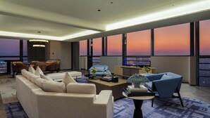 Una sala moderna con sofá, sillones, una mesa de centro y vistas a la puesta de sol a través de amplias ventanas.