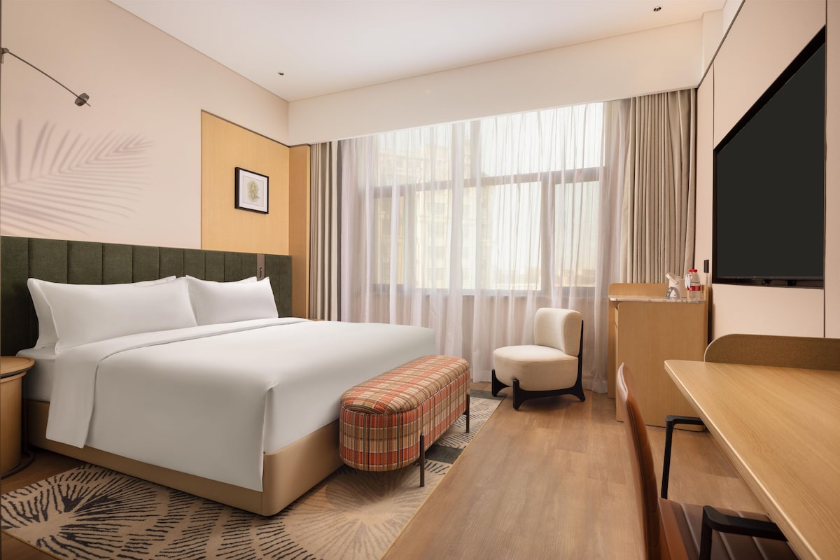 Una habitación de hotel con una cama grande, una mesita, una silla, un escritorio y un televisor.