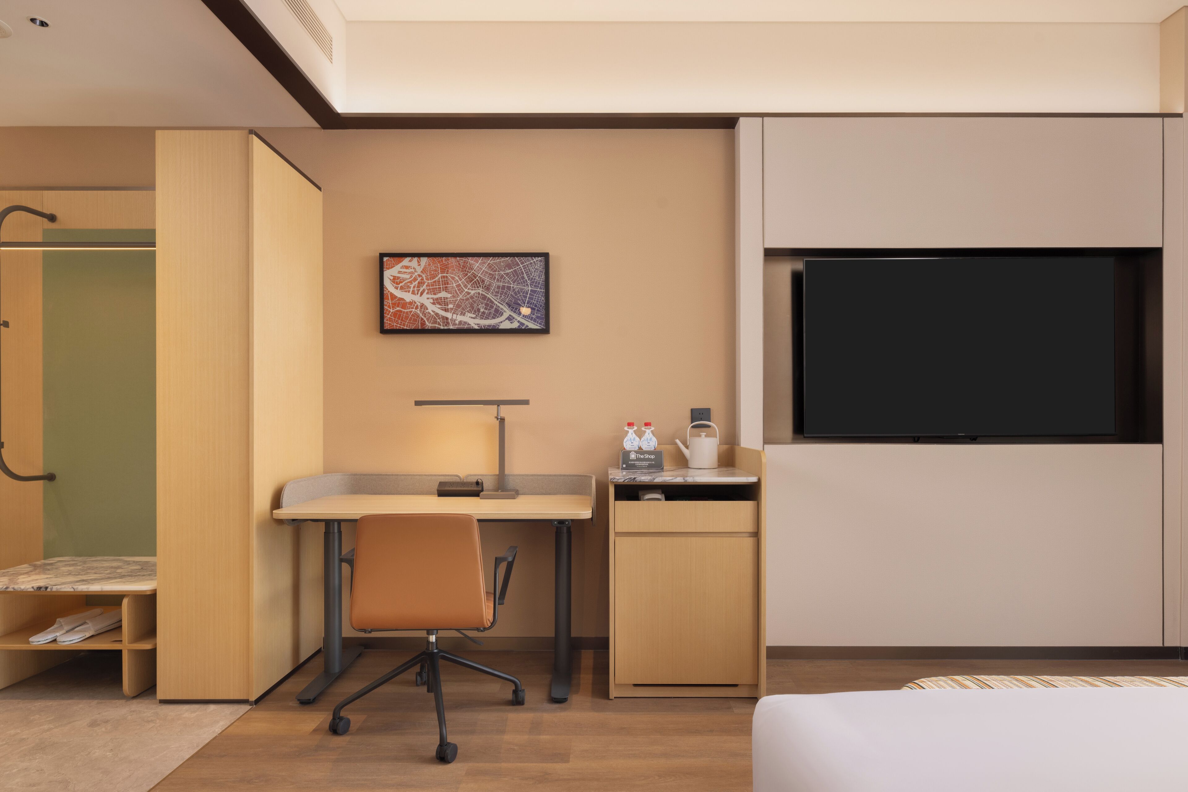 A hotel room with a bed, a desk with a chair, a flat-screen TV, a small cabinet, and a wall-mounted artwork.