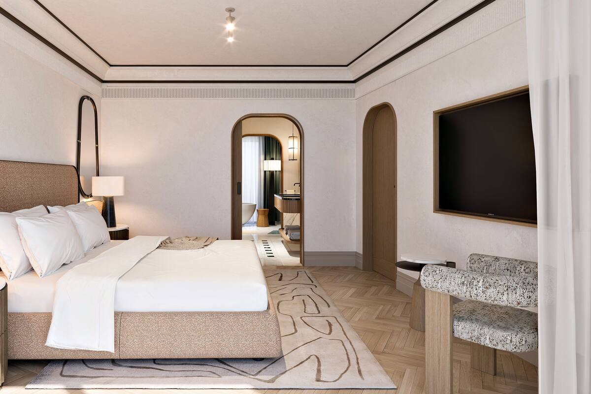 A modern hotel room with a large bed, a desk, a chair, and a television.
