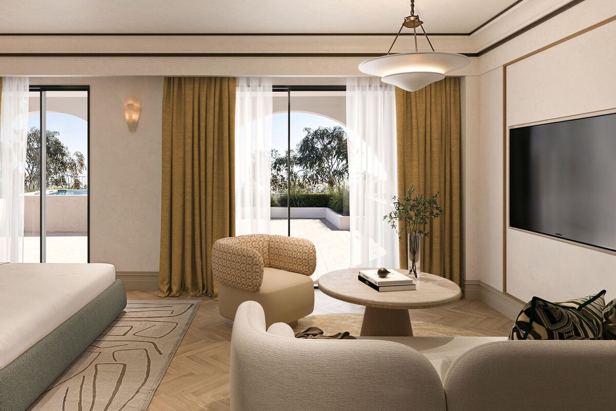 A hotel room with a bed, a sofa, a coffee table, a TV, and a view of the outdoors.
