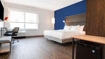 Une chambre d’hôtel équipée d’un lit, d’un bureau, d’une chaise et d’un petit réfrigérateur.