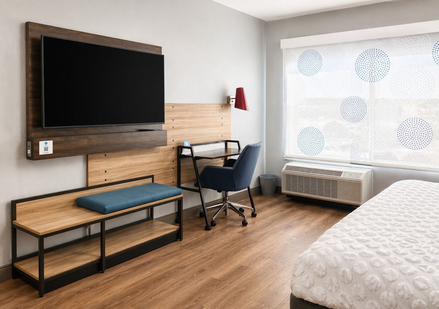 Une chambre d’hôtel équipée d’une télévision à écran plat, d’un bureau avec une chaise, d’un banc, d’un lit et d’une grande fenêtre donnant sur un paysage agréable.