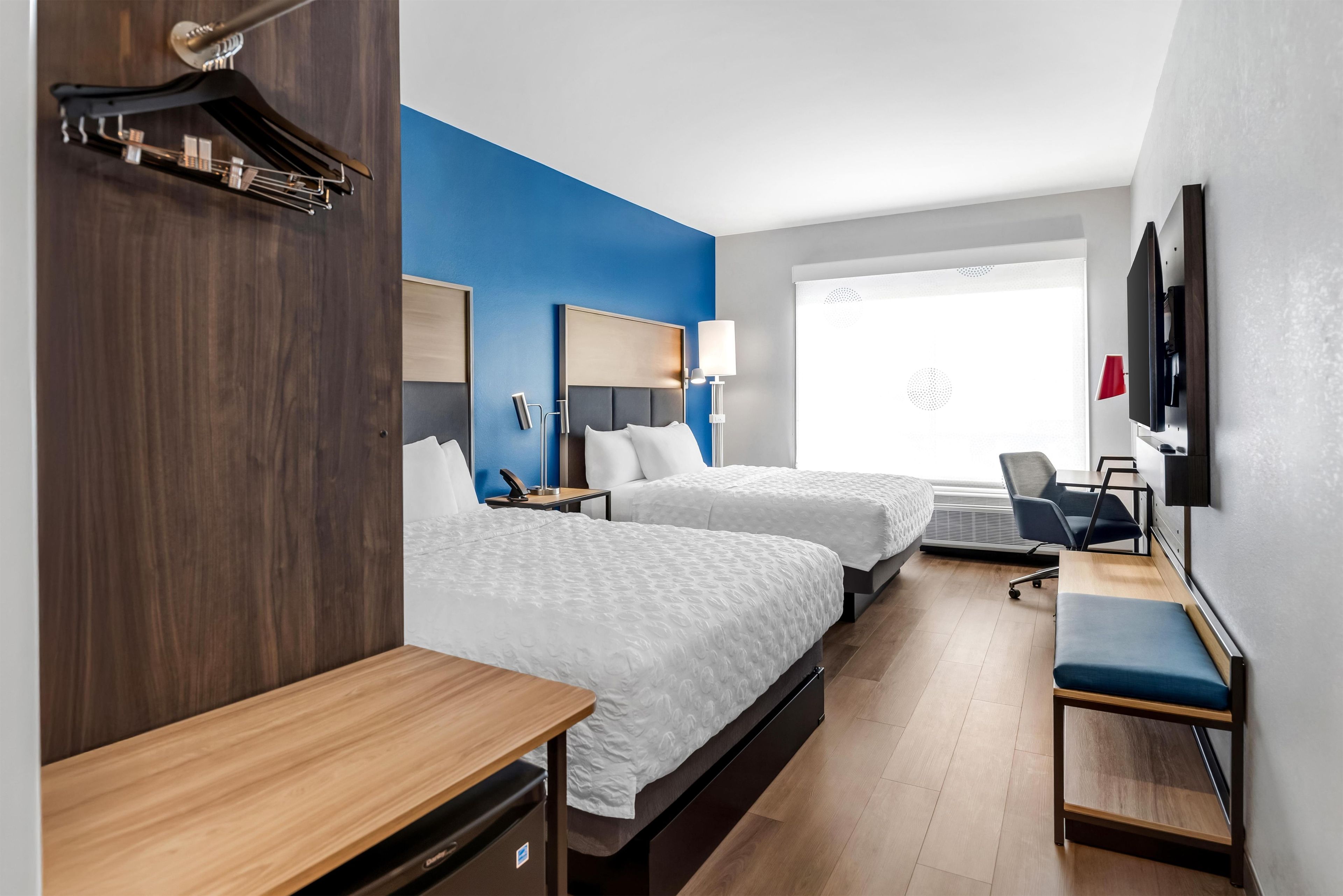 A hotel room with two beds, a desk, a chair, a TV, and a window with blinds.