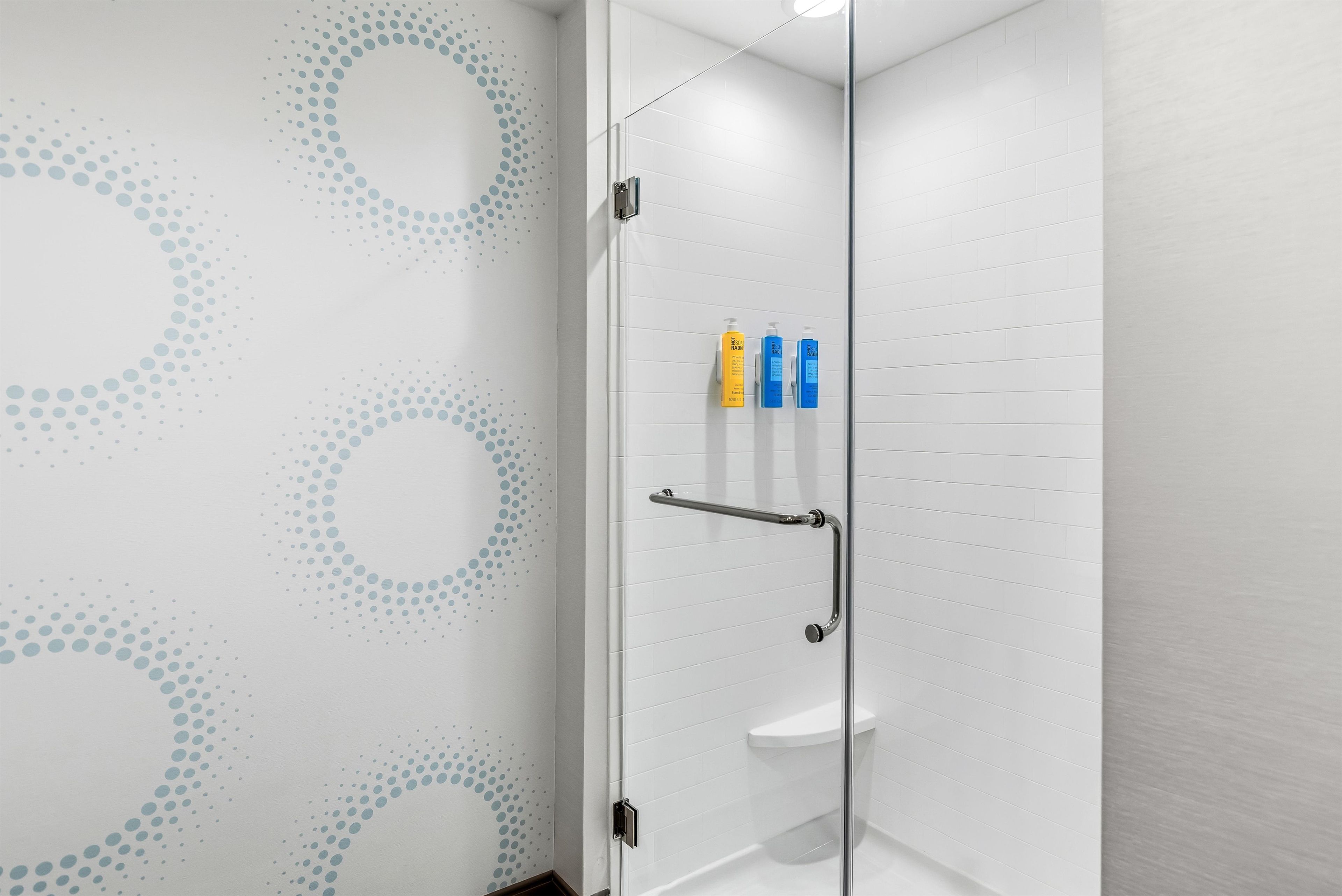 A modern bathroom with a glass shower enclosure, white tiled walls, and a decorative wall pattern.
