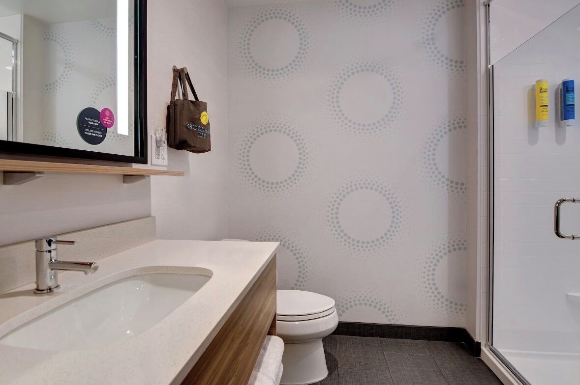 A bathroom with a sink, toilet, and shower. A brown bag hangs on the wall.