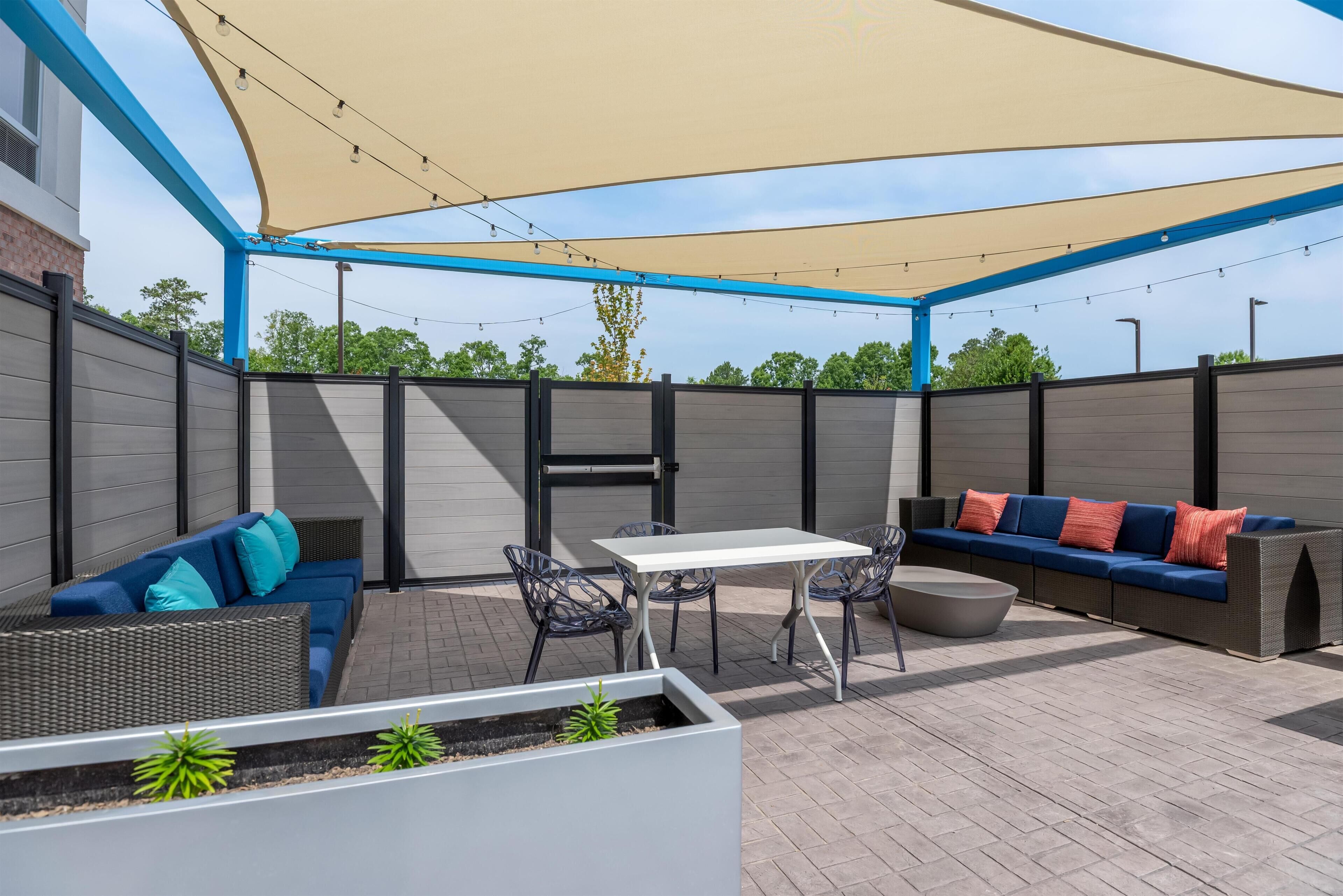 An outdoor patio with a table, chairs, a sofa, and a shaded area.