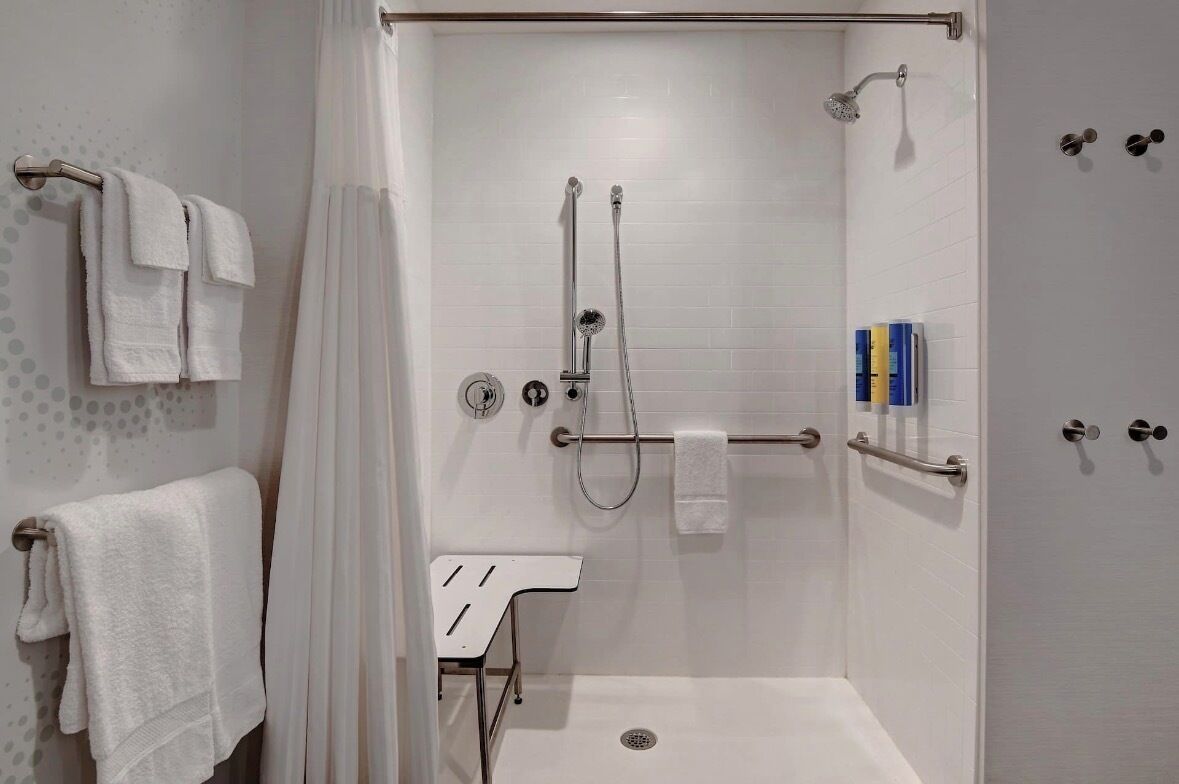 Ducha a pie con mampara de vidrio, un perchero, una mesita y un panel de control de la ducha.