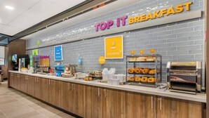 Un comptoir où l’on sert le petit-déjeuner, avec une pancarte indiquant « PETIT-DÉJEUNER À VOLONTÉ », une variété de produits de boulangerie et une machine à café.