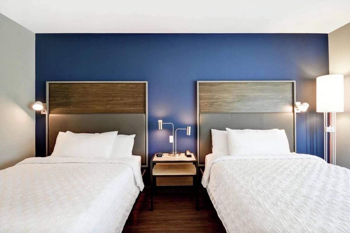 Ein Hotelzimmer mit zwei Betten, einem Nachttisch mit Lampe und einer Wandleuchte.