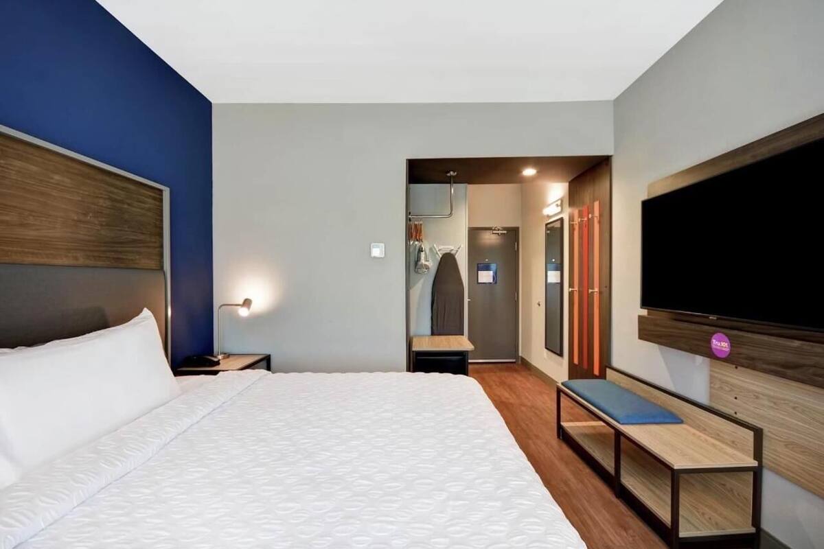 Ein Hotelzimmer mit Bett, Sitzbank, Fernseher, Kleiderschrank und Spiegel.