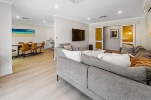 Ein modernes Wohnzimmer mit einem grauen Sofa, einem Essbereich mit Tisch und Stühlen sowie einem an der Wand montierten Flachbildfernseher.