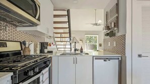 Una cocina moderna con estufa a gas, armarios blancos, microondas y un refrigerador pequeño.