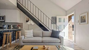 Una sala de estar moderna con un sofá gris, una mesa de centro de madera y una escalera que conduce a un piso superior.