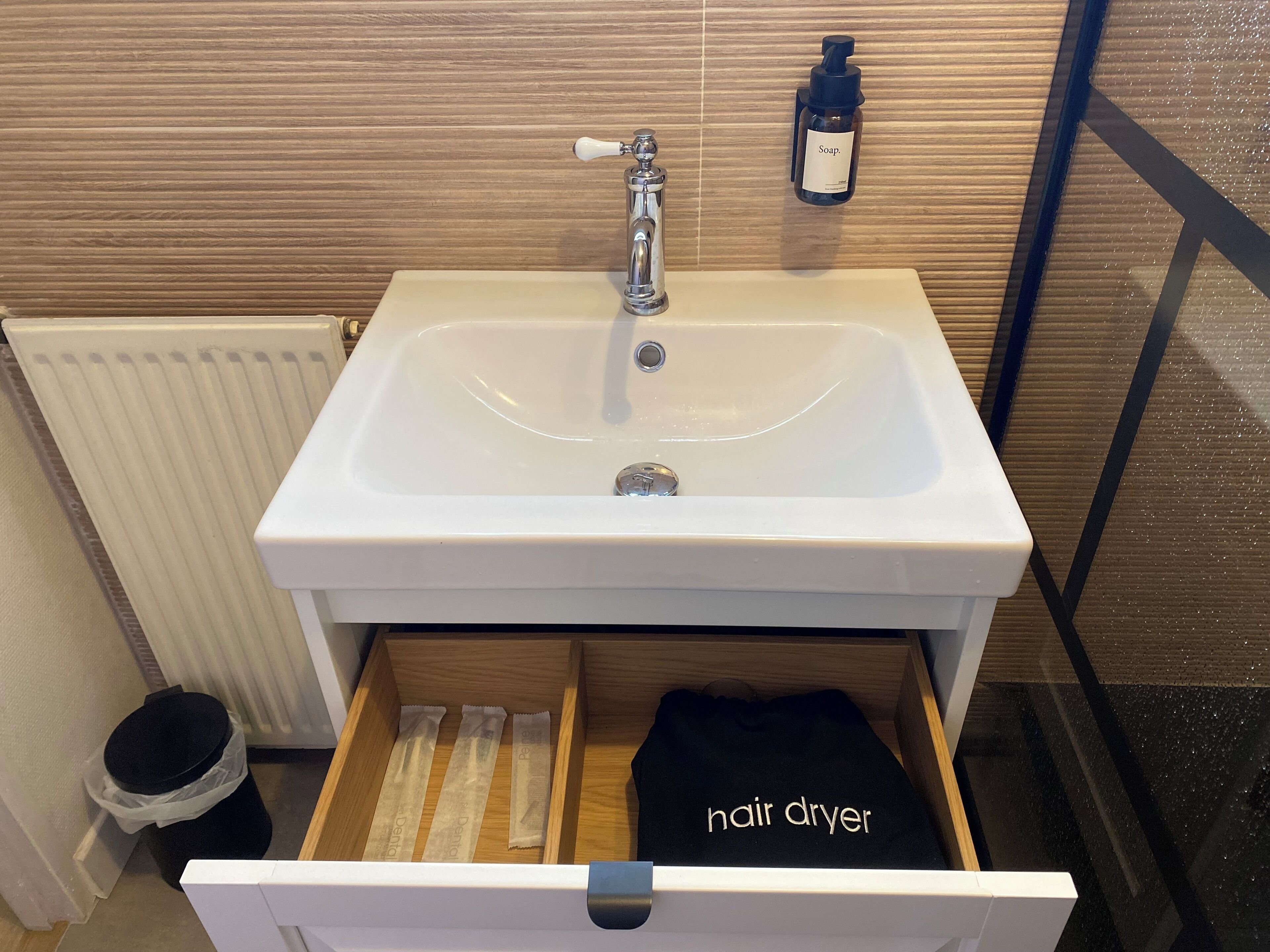 A bathroom with a white sink, a bottle of soap, and a drawer containing a hair dryer.