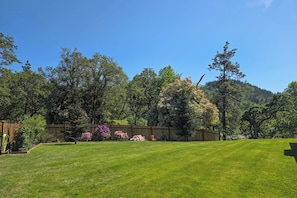 A well-maintained grassy yard with a wooden fence, surrounded by trees and flowering plants. - Walk to River: Myrtle Creek Studio Near I-5 (Myrtle Creek)