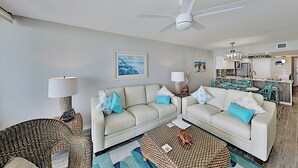 Ein Wohnzimmer mit zwei Sofas, einem Deckenventilator und einer Küche im Hintergrund.