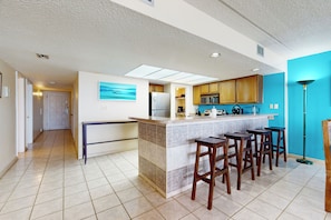 A modern kitchen with a central island, bar stools, and a view of the hallway. - 3BR w/ Gulf Views & Pool: Suntide III - Unit 808 (South Padre Island)