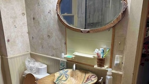 A bathroom with a wooden vanity, a round mirror, a toilet, and a sink with a decorative bowl. - This 1889 house is one of the most historic and unique places in Canon city. (Cañon City)