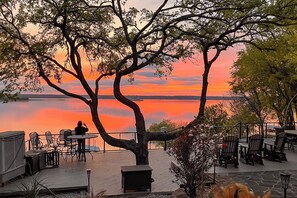 A lakeside patio with outdoor seating and a view of the sunset. - Lakefront Estate: Stunning Views, Deck, Bar & Dock (Bridgeport)