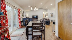 A dining area with a wooden table and chairs, a chandelier, and a television in the background. - 1/2 Mi to Lake! Traverse City Retreat w/ Dock (Traverse City)