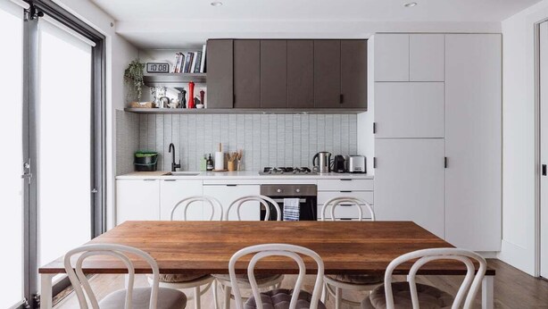 A modern kitchen with white cabinets, a wooden dining table, and four white chairs. - The Carlton Residences (Melbourne)