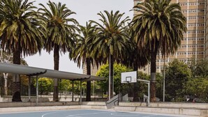 An outdoor basketball court with a basketball hoop, surrounded by palm trees and a building in the background. - The Carlton Residences (Melbourne)