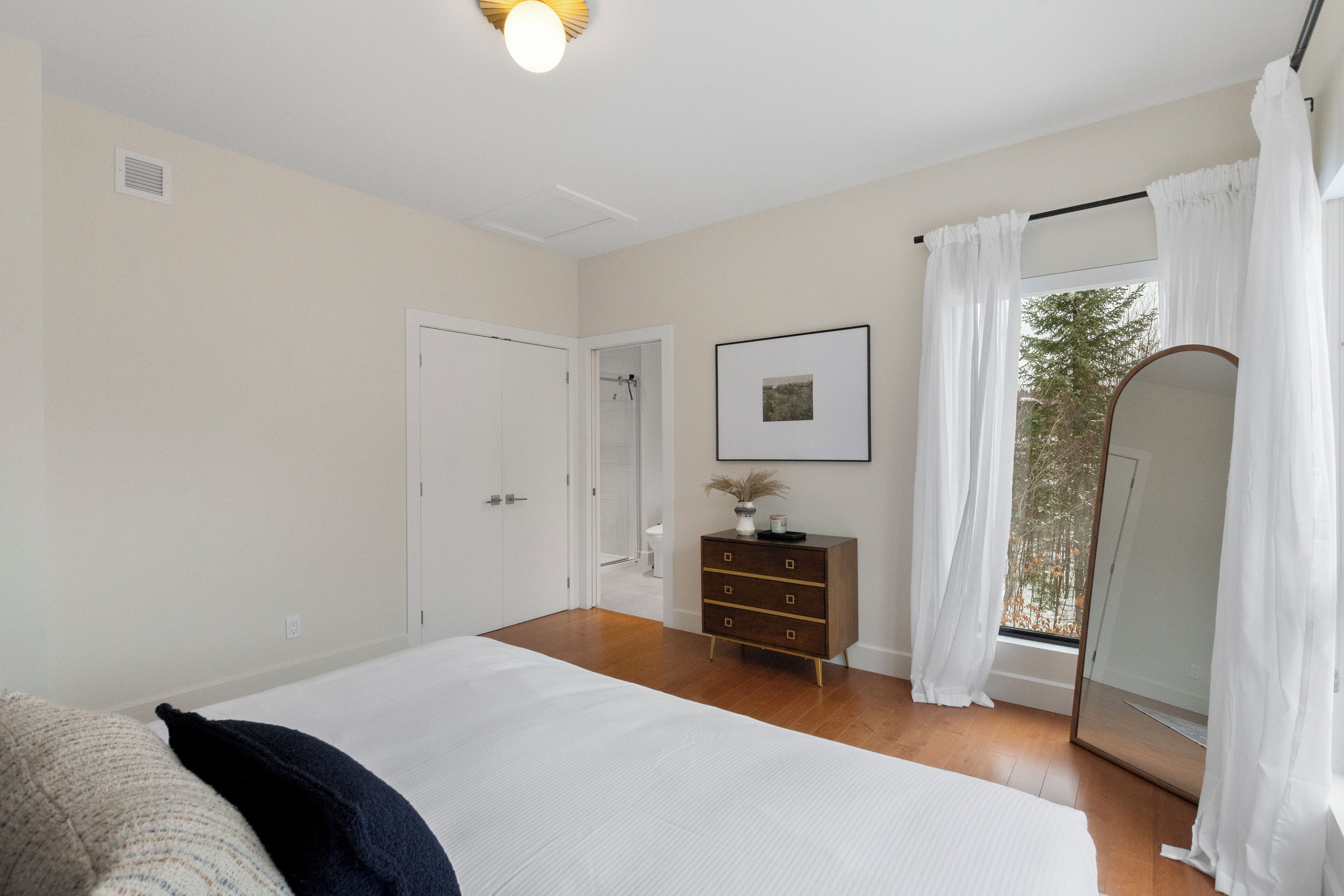 A bedroom with a large bed, a dresser, a framed picture on the wall, and a window with curtains.