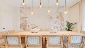 Un espace repas comprenant une table ronde, six chaises en osier et des lampes suspendues.