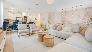 Un salon moderne avec un canapé, des fauteuils, une table basse et une cuisine en arrière-plan.