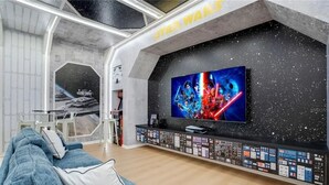 Un salon moderne avec un mur décoré sur le thème de Star Wars, un grand téléviseur à écran plat et un panneau de contrôle original placé sous le téléviseur.