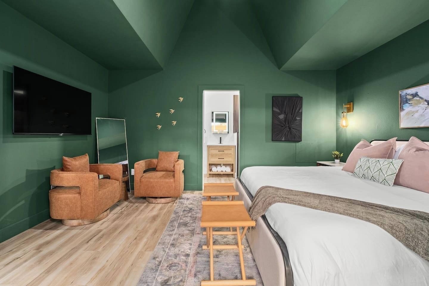 A bedroom with a bed, two armchairs, a TV, and a dresser.