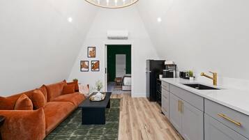 A modern loft apartment with a living area, kitchen, and a green door leading to a bedroom.