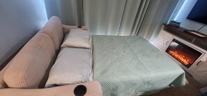 Una habitación acogedora con sofá, cama con colcha, chimenea y televisor sobre un mueble.