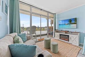 A modern living room with a sofa, ottomans, a fireplace, and a TV. - Oceanfront Condo*Walkout Patio Beach Access*Steps to the Sea* (North Myrtle Beach)