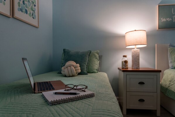 A bedroom with a bed, a bedside table with a lamp, a laptop, a notebook, and a plush toy. - Oceanfront Condo*Walkout Patio Beach Access*Steps to the Sea* (North Myrtle Beach)