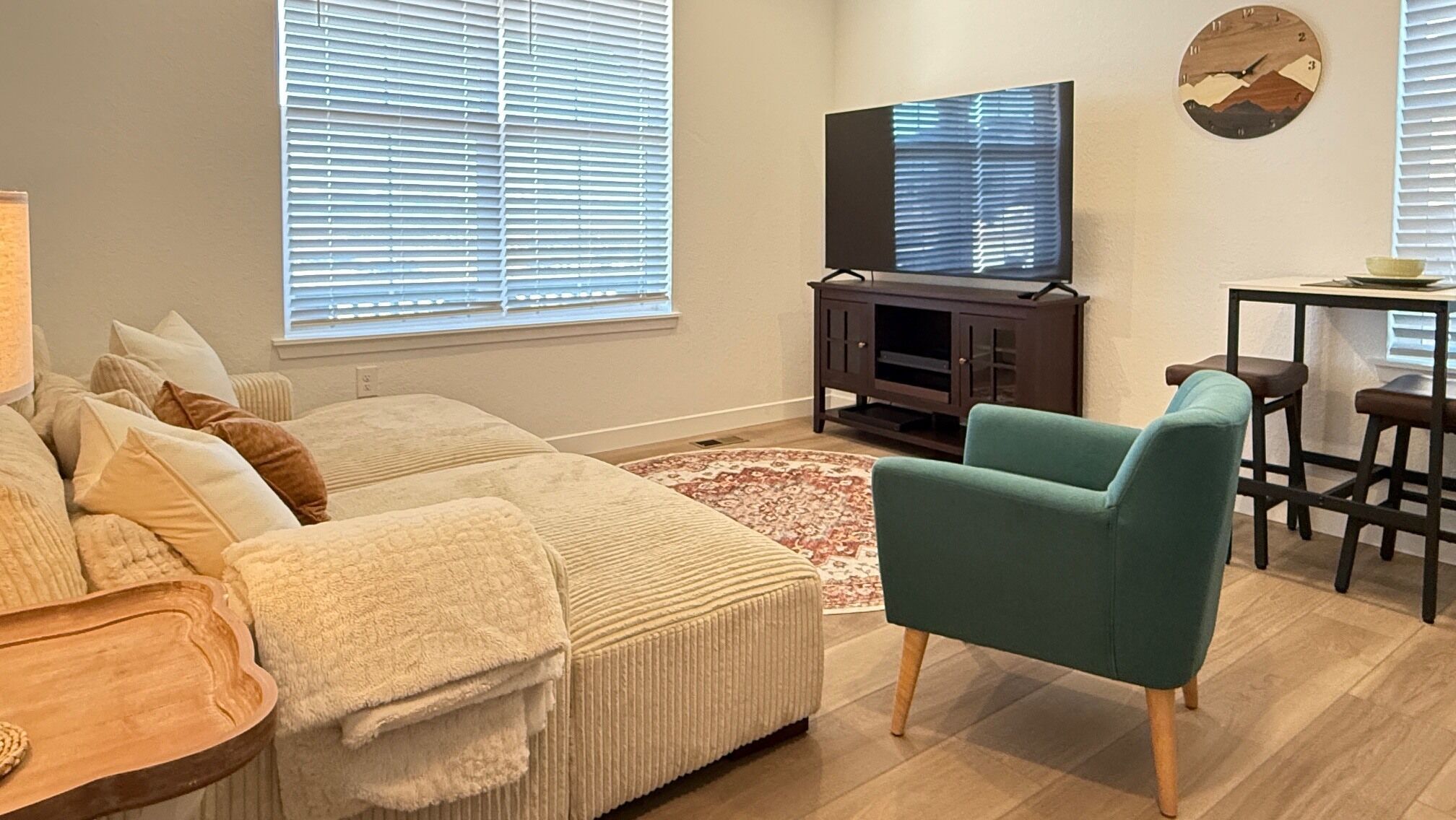 Un salon comprenant un canapé, un fauteuil turquoise, un téléviseur et un coin repas avec une table et des chaises.