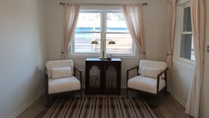 Una habitación con dos sillas, una mesita y un ventanal con cortinas.