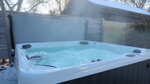 Un jacuzzi con un muelle de madera que lo rodea, una escalera y una cerca de madera al fondo.