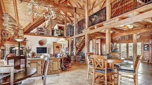 A spacious log cabin interior with a dining area, kitchen, and a staircase leading to a loft. - Breathtaking Log Home w/Panoramic Mountain Views, Hot Tub, 2 Game rooms, 6 bdrms (Angel Fire)