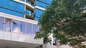 A modern building with a glass facade, a landscaped area with a fountain, and a gated entrance. - Central Waikiki  Bch Gear, Parking, Kitchen, King (Honolulu)