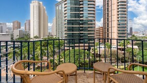 A balcony with wicker chairs, overlooking a cityscape with tall buildings and palm trees. - Central Waikiki  Bch Gear, Parking, Kitchen, King (Honolulu)