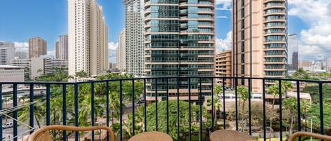 A balcony with wicker chairs, overlooking a cityscape with tall buildings and palm trees.