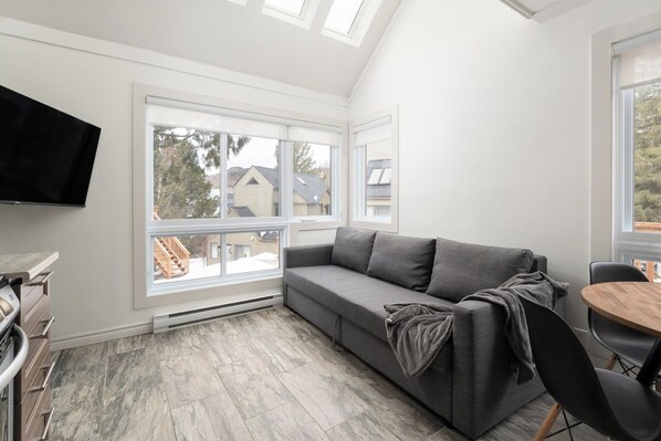 Una sala de estar moderna con un sofá gris, un televisor de pantalla plana y un comedor con una mesa y sillas de madera.